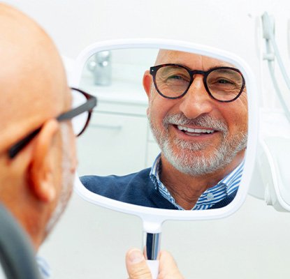 A man smiling at his dental implants in a mirror