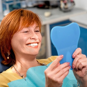 Woman with dentures smiling into hand mirror
