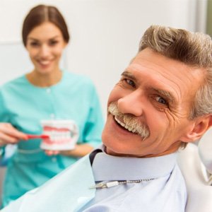 Older man with dental implants smiles as he leans back in the examination chair