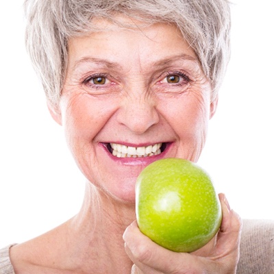 woman with a dental implant holding an apple