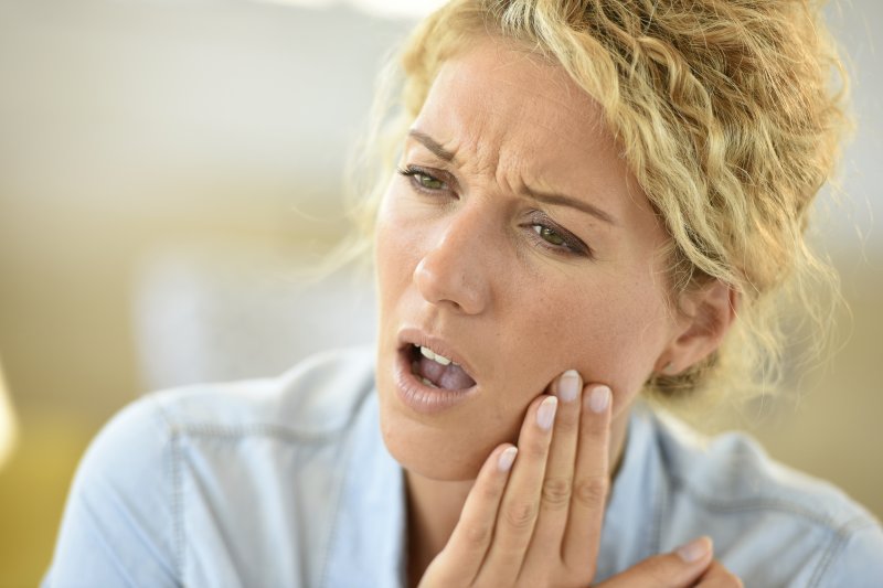 Blonde woman with toothache rubbing her jaw