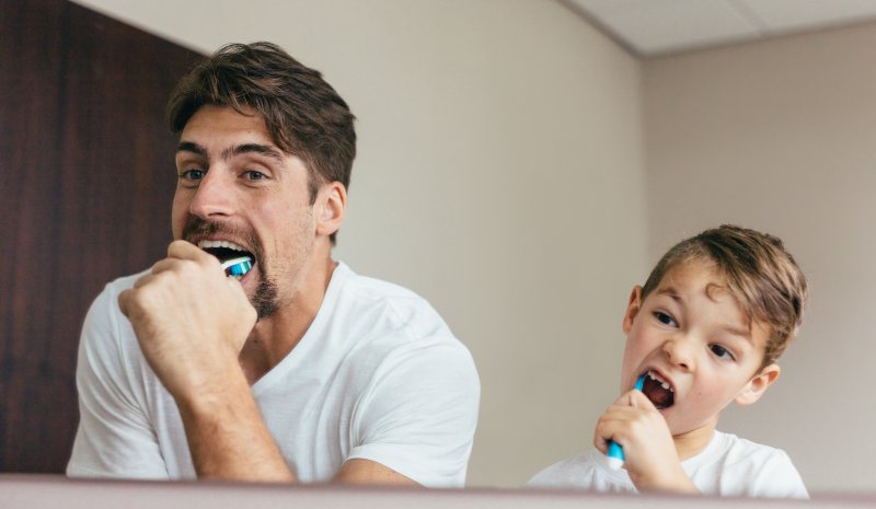 Father and son brushing teeth in bathroom mirror